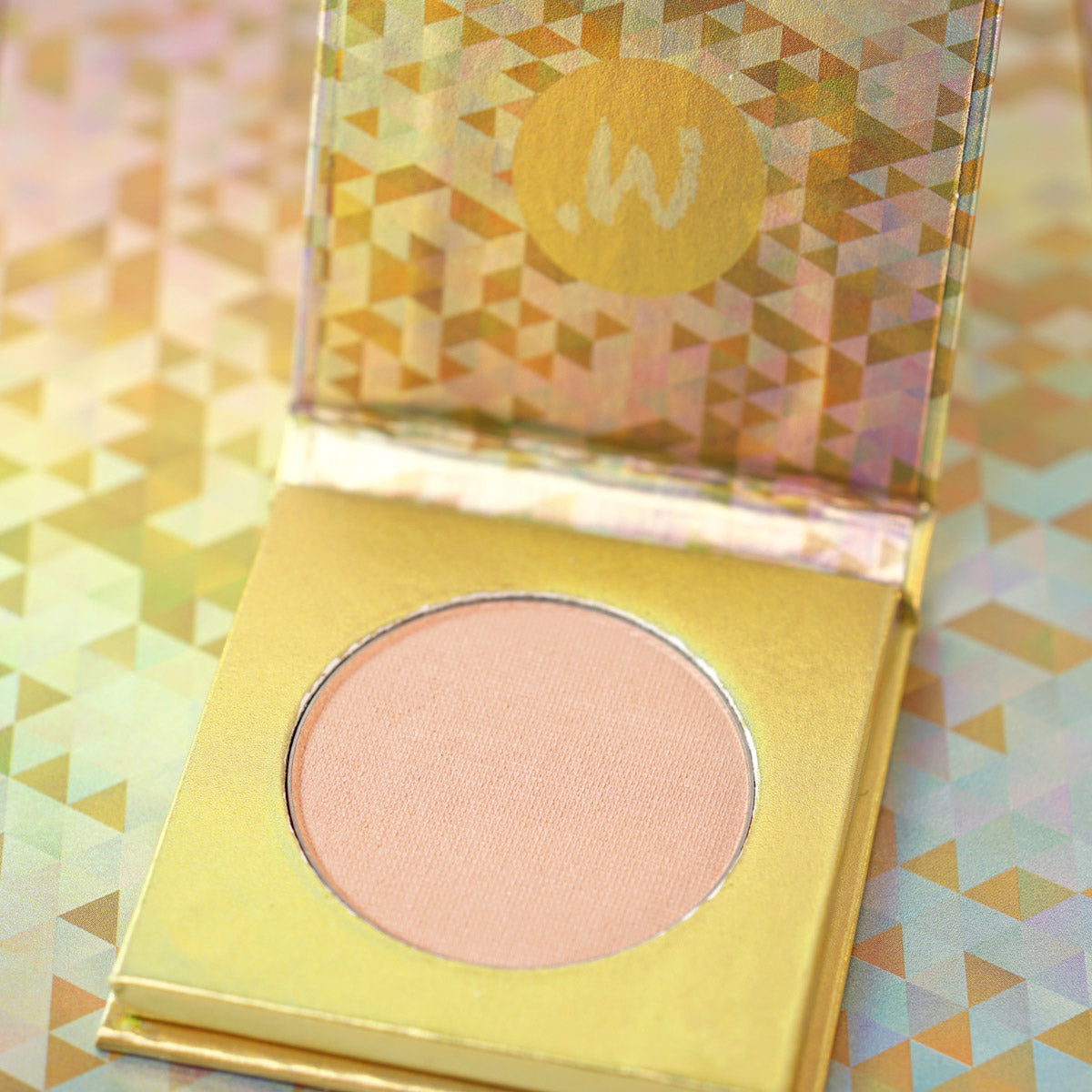 A close-up of a pressed powder blush in a peach shade, with the brand logo visible on the compact case.